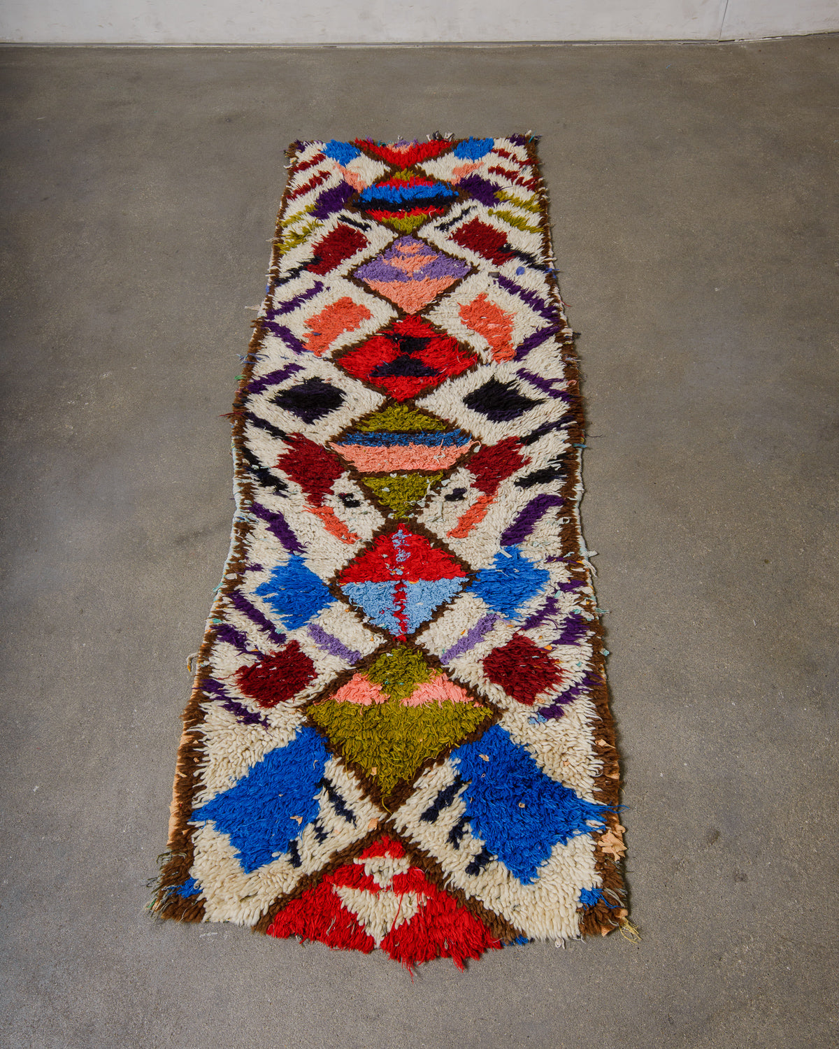 Colourful boucherouite rug laying on concrete floor.